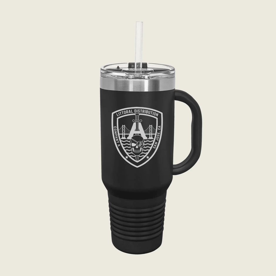 A matte black insulated travel tumbler with a clear lid and straw, featuring a white shield logo on the front with a skull and bridge graphic, set against a solid light beige background.