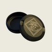 Round black container with gold lid featuring a logo on a beige background