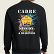 A person shown from the back wearing a black crewneck sweatshirt with a large graphic print. The graphic features the text 'CADRE' and 'MISSION Motherhood & READINESS' in white and yellow, surrounded by a yellow badge design with pink and blue paint splatters on a light beige background.