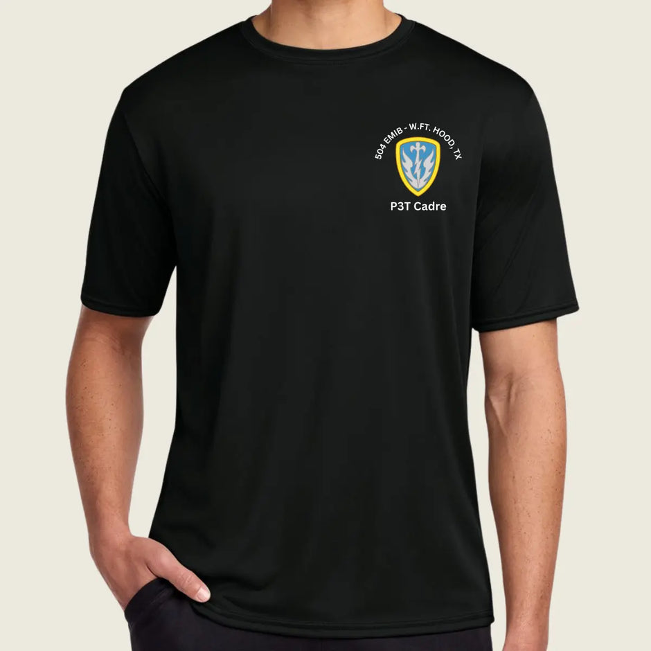 A man wearing a black short-sleeve crewneck t-shirt with a small military-style crest on the left chest. The crest features a yellow and blue shield with white text reading Cadre'.