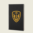 A black hardcover notebook featuring a gold shield emblem with a sword, lightning bolt, and flame design on the front cover, set against a solid light beige background.