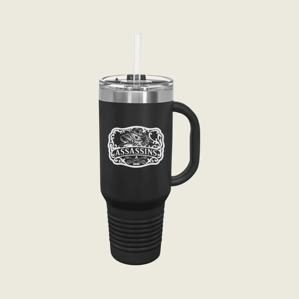 A black insulated travel tumbler with a handle, clear lid, and white straw, featuring a white graphic print that reads 'ASSASSINS' The tumbler is centered on a light beige background.