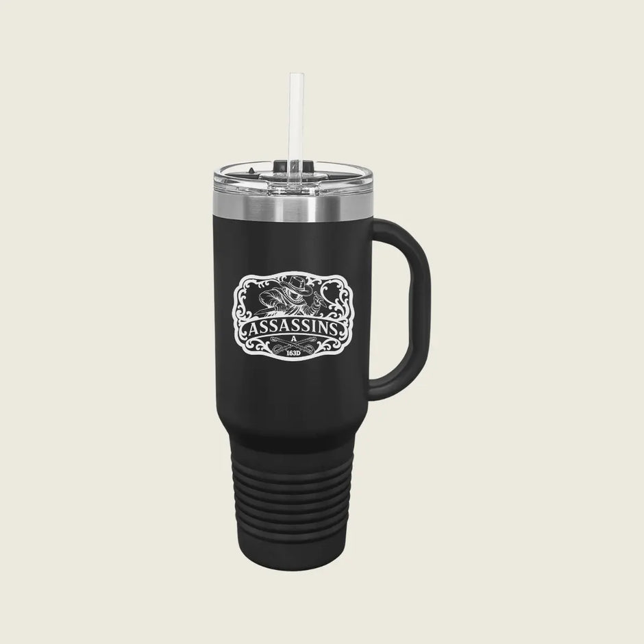 A black insulated travel tumbler with a handle, clear lid, and white straw, featuring a white graphic print that reads 'ASSASSINS' The tumbler is centered on a light beige background.