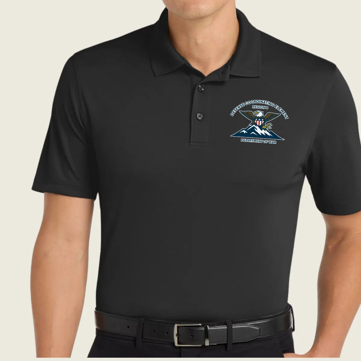 A man wearing a black short-sleeve polo shirt with a custom logo printed on the left chest, paired with a black belt against a light beige background.