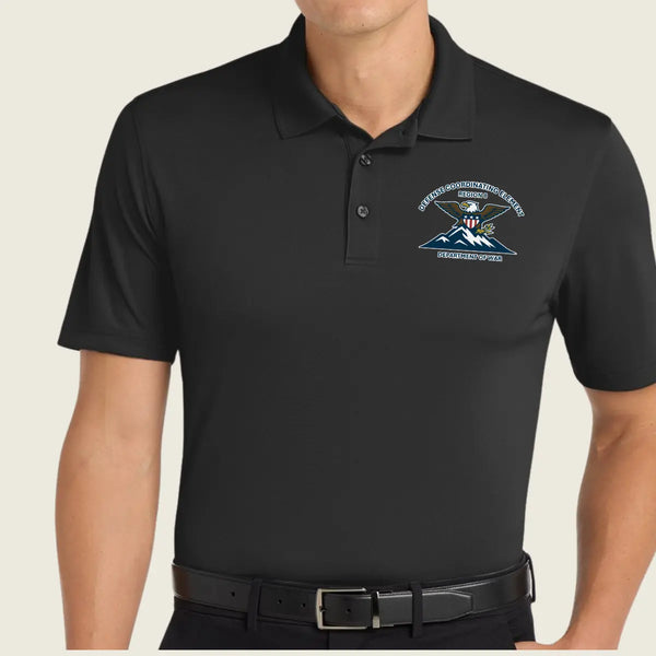 A man wearing a black short-sleeve polo shirt with a custom logo printed on the left chest, paired with a black belt against a light beige background.
