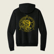 A black pullover hoodie shown from the back, featuring a large yellow graphic print of an astronaut inside a triangle emblem with the text 'Marine Cryptologic Support Mission Company A' on a light beige background.
