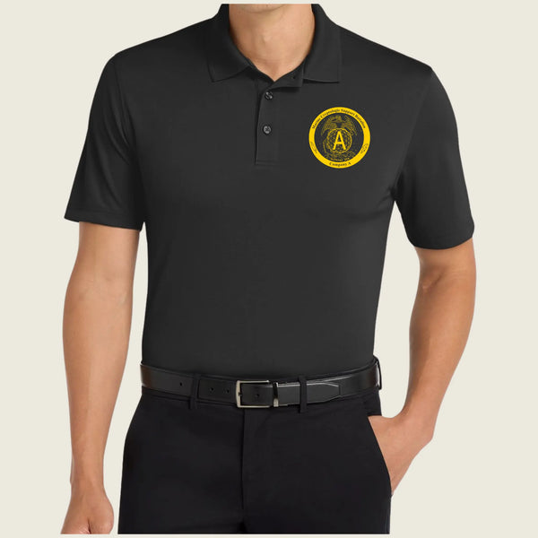 A man wearing a black short-sleeve polo shirt with a yellow circular 'A' emblem on the left chest, paired with black trousers and a black belt, against a light beige background.