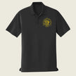 A black short-sleeve polo shirt with a gold circular emblem printed on the left chest, displayed on a solid light beige background.