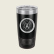 A black insulated travel tumbler with a clear lid, featuring a circular white graphic on the front with a central letter A and decorative text.