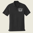 A black short-sleeve polo shirt with a white embroidered logo on the left chest reading 'BATTERY Q 5/14 AURORA, CO' around crossed tools, shown on a light beige background.