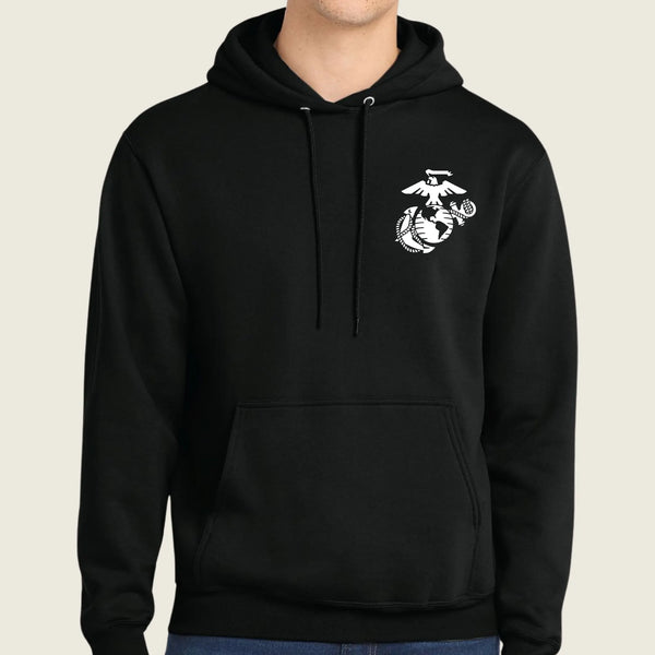 A black pullover hoodie with a white US Marine Corps Eagle, Globe, and Anchor emblem printed on the left chest, worn by a model against a light beige background.