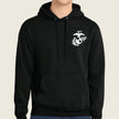 A black pullover hoodie with a white US Marine Corps Eagle, Globe, and Anchor emblem printed on the left chest, worn by a model against a light beige background.