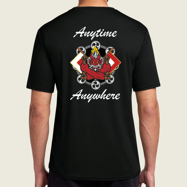 A man wearing a black short-sleeve t-shirt, viewed from the back. The shirt features a large graphic print in the center with a red demon face, soccer balls, and the words 'Anytime Anywhere' in white script.