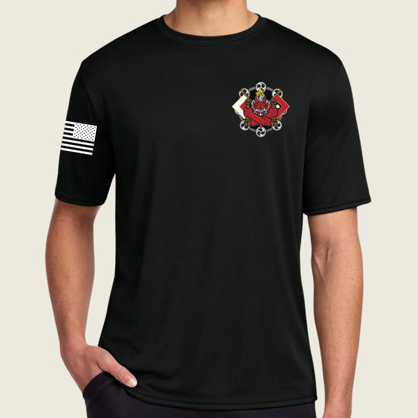 A man wearing a black short-sleeve t-shirt with a small red and white graphic on the left chest and a black-and-white American flag graphic on the right sleeve, shown against a light beige background.