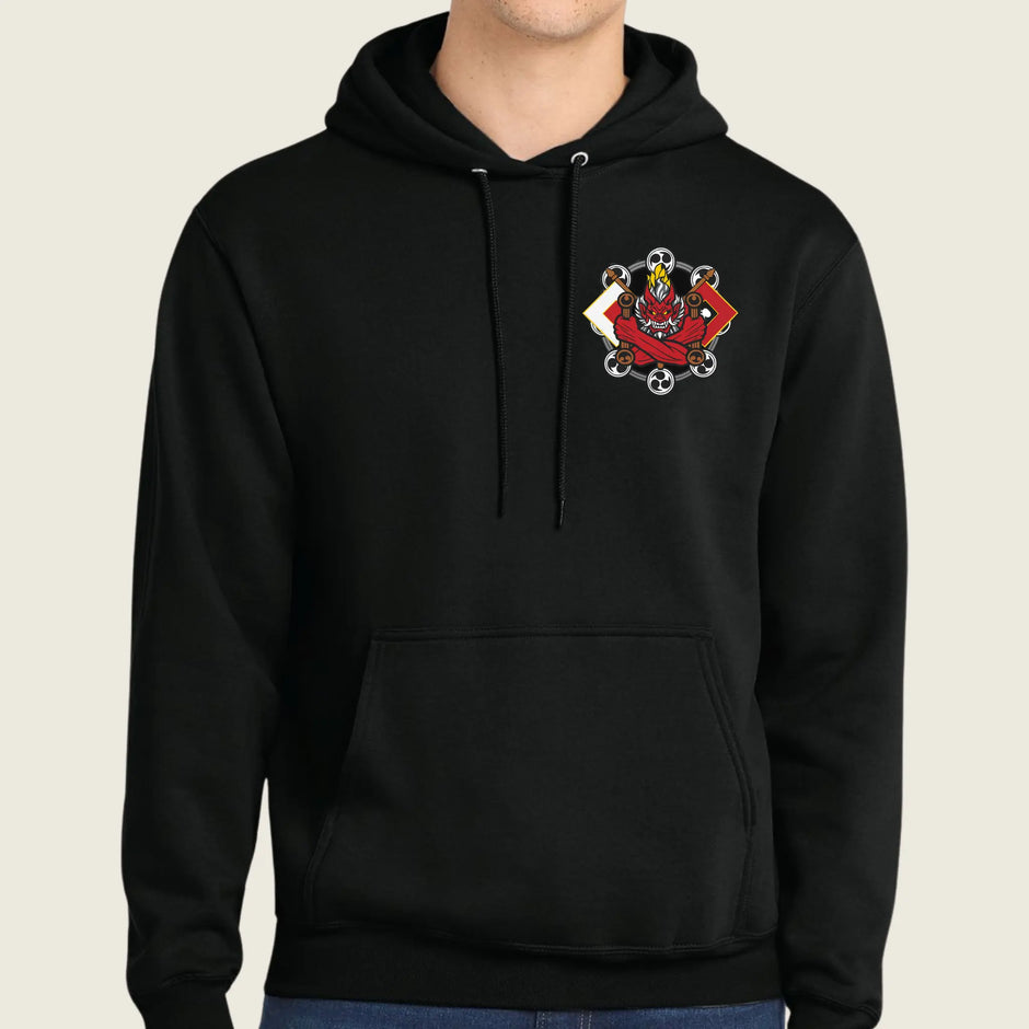 A black pullover hoodie with a small red and white graphic on the left chest, worn by a model against a light beige background.