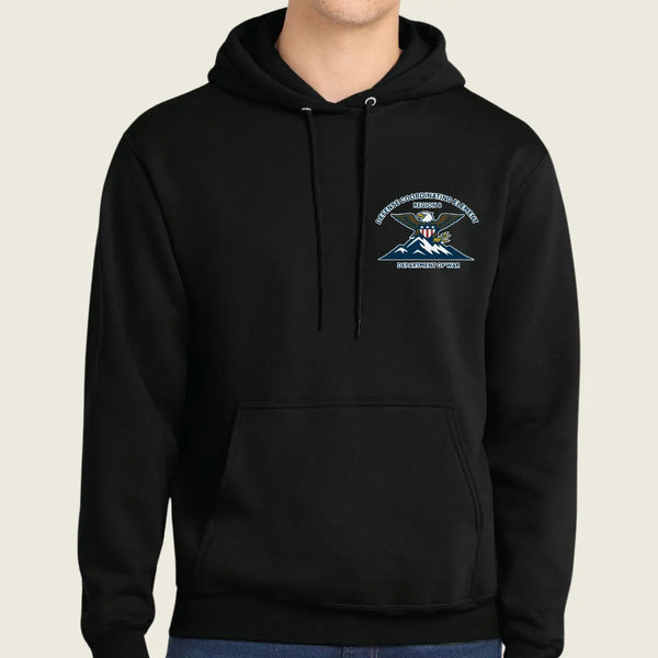 A person wearing a black pullover hoodie with a small logo on the left chest, shown against a plain light beige background.