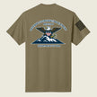 An coyote brown short-sleeve t-shirt shown from the back, featuring a large military-style graphic of an eagle over mountains with the text 'DEFENSE COORDINATING ELEMENT REGION 8' and 'DEPARTMENT OF WAR'. A black striped flag-style patch is printed on the left sleeve.