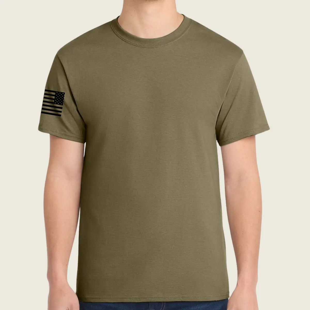An coyote brown t-shirt worn by a model, featuring a black distressed American flag graphic on the left sleeve, set against a solid light beige background.