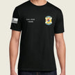A man wearing a black short-sleeve t-shirt with a black-and-white American flag graphic on the right sleeve, white placeholder text reading 'CALL SIGN / NAME' on the right chest, and a colorful badge graphic on the left chest, shown against a light beige background.