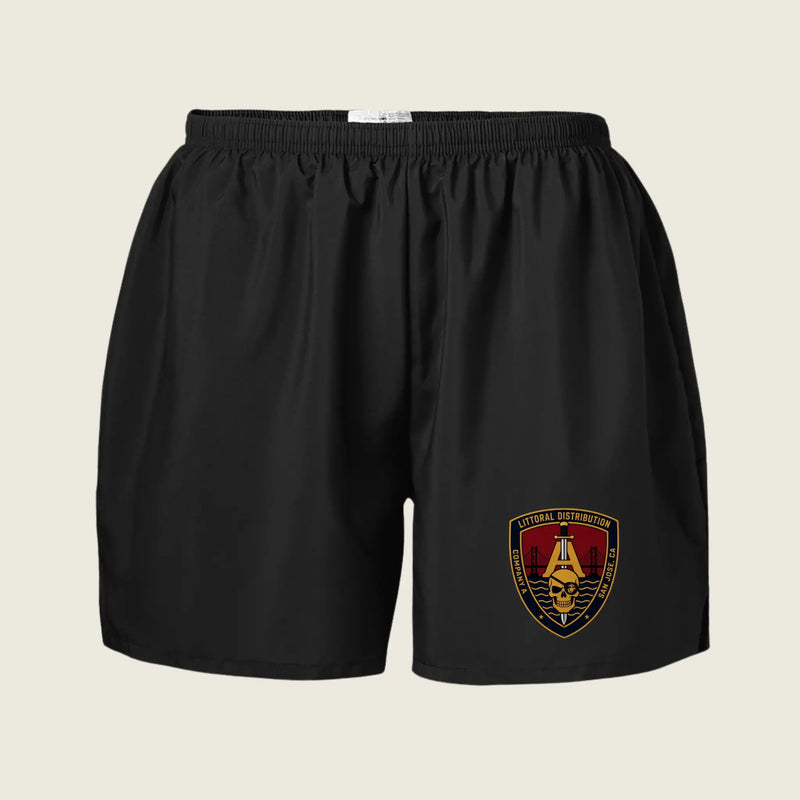 Black athletic shorts with an elastic waistband and a military-style crest patch on the lower left leg, displayed against a light beige background.