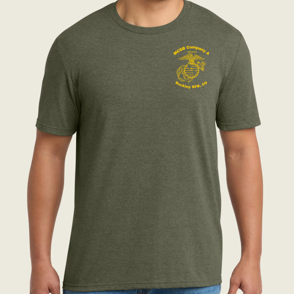 A man wearing a heather olive green crewneck t-shirt with a yellow US Marine Corps Eagle, Globe, and Anchor emblem printed on the left chest, paired with blue jeans.