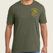 A man wearing a heather olive green crewneck t-shirt with a yellow US Marine Corps Eagle, Globe, and Anchor emblem printed on the left chest, paired with blue jeans.