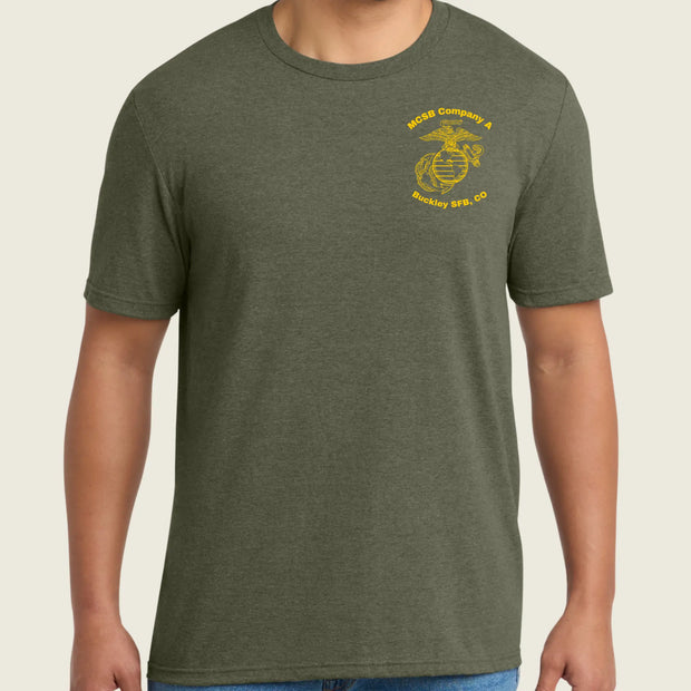A man wearing a heather olive green crewneck t-shirt with a yellow US Marine Corps Eagle, Globe, and Anchor emblem printed on the left chest, paired with blue jeans.