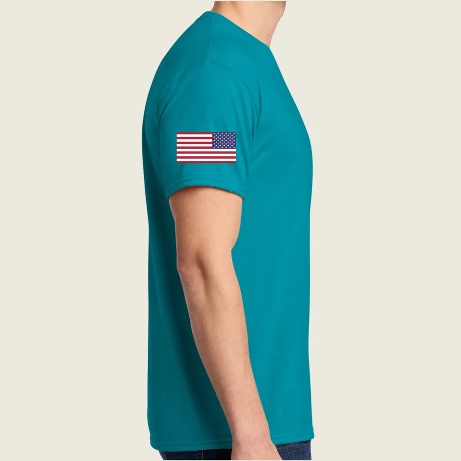 A man wearing a teal short-sleeve t-shirt with a small American flag printed on the left sleeve, shown from a side profile against a light beige background.