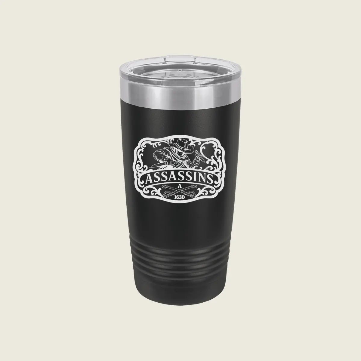A black insulated travel tumbler with a clear lid and a white 'Assassins' graphic on the front, set against a solid light beige background.