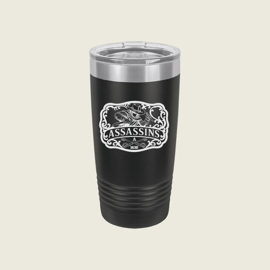 A black insulated travel tumbler with a clear lid and a white 'Assassins' graphic on the front, set against a solid light beige background.