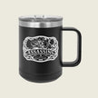 A black insulated travel mug with a clear lid and black handle, featuring a white 'Assassins' graphic on the front, set against a solid light beige background.