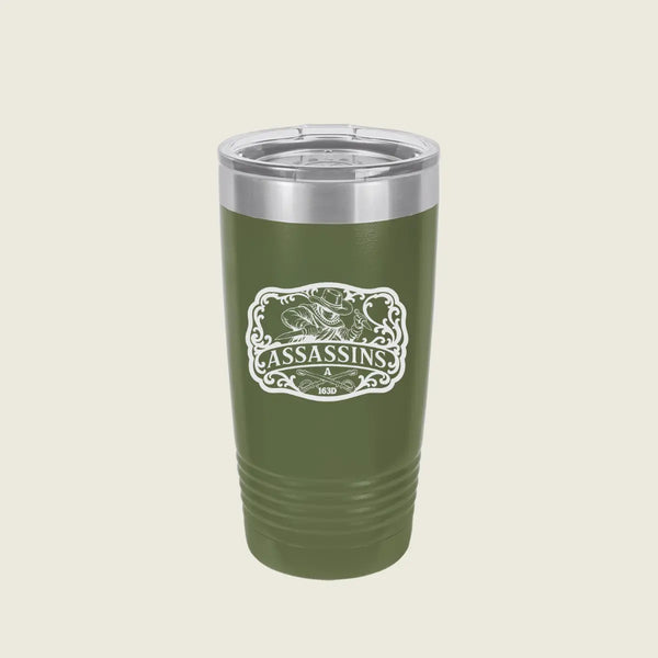 A green insulated travel tumbler with a clear lid and a white 'Assassins' graphic on the front, set against a solid light beige background.