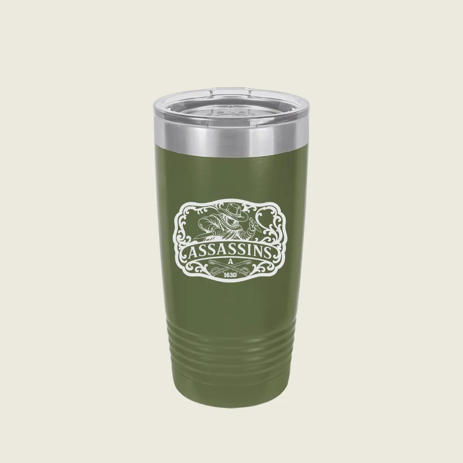 A green insulated travel tumbler with a clear lid and a white 'Assassins' graphic on the front, set against a solid light beige background.