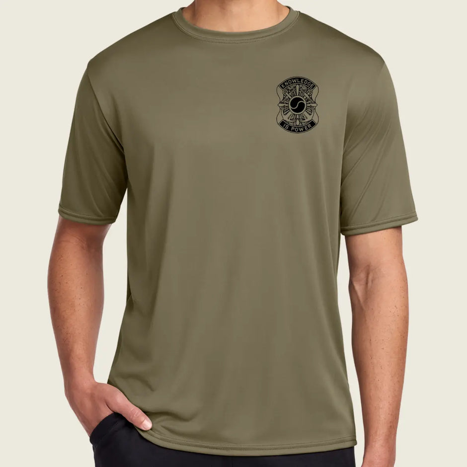 Person wearing a coyote brown t-shirt with a logo on the chest against a beige background