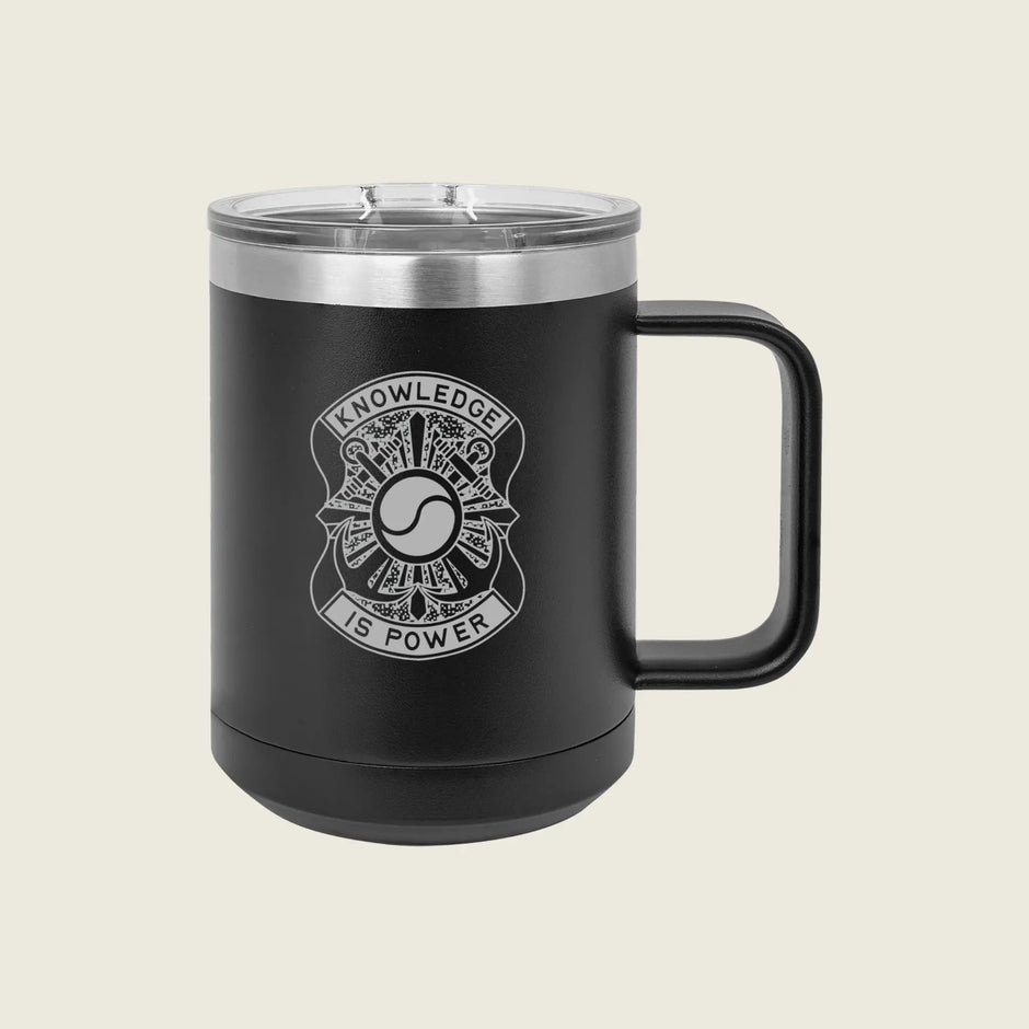 A matte black insulated travel mug with a clear lid and a black handle, featuring a white graphic design on the front that reads 'KNOWLEDGE IS POWER' around a circular emblem. The mug is photographed against a solid, light beige background.