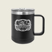 A black insulated travel mug with a clear lid and a black handle, featuring a white graphic design on the front with the word 'ASSASSINS' and a stylized illustration, set against a light beige background.