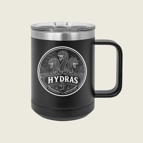 A black insulated travel mug with a clear lid and a black handle, featuring a circular silver graphic of three serpents and the word 'HYDRAS' on the front, set against a light beige background.