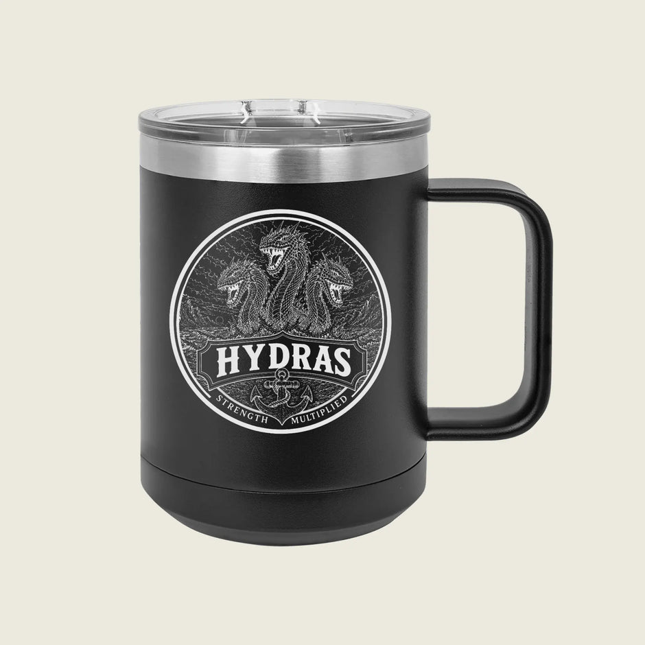 A black insulated travel mug with a clear lid and a black handle, featuring a circular silver graphic of three serpents and the word 'HYDRAS' on the front, set against a light beige background.