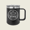 A black insulated travel mug with a clear lid and a black handle, featuring a circular silver graphic of three serpents and the word 'HYDRAS' on the front, set against a light beige background.