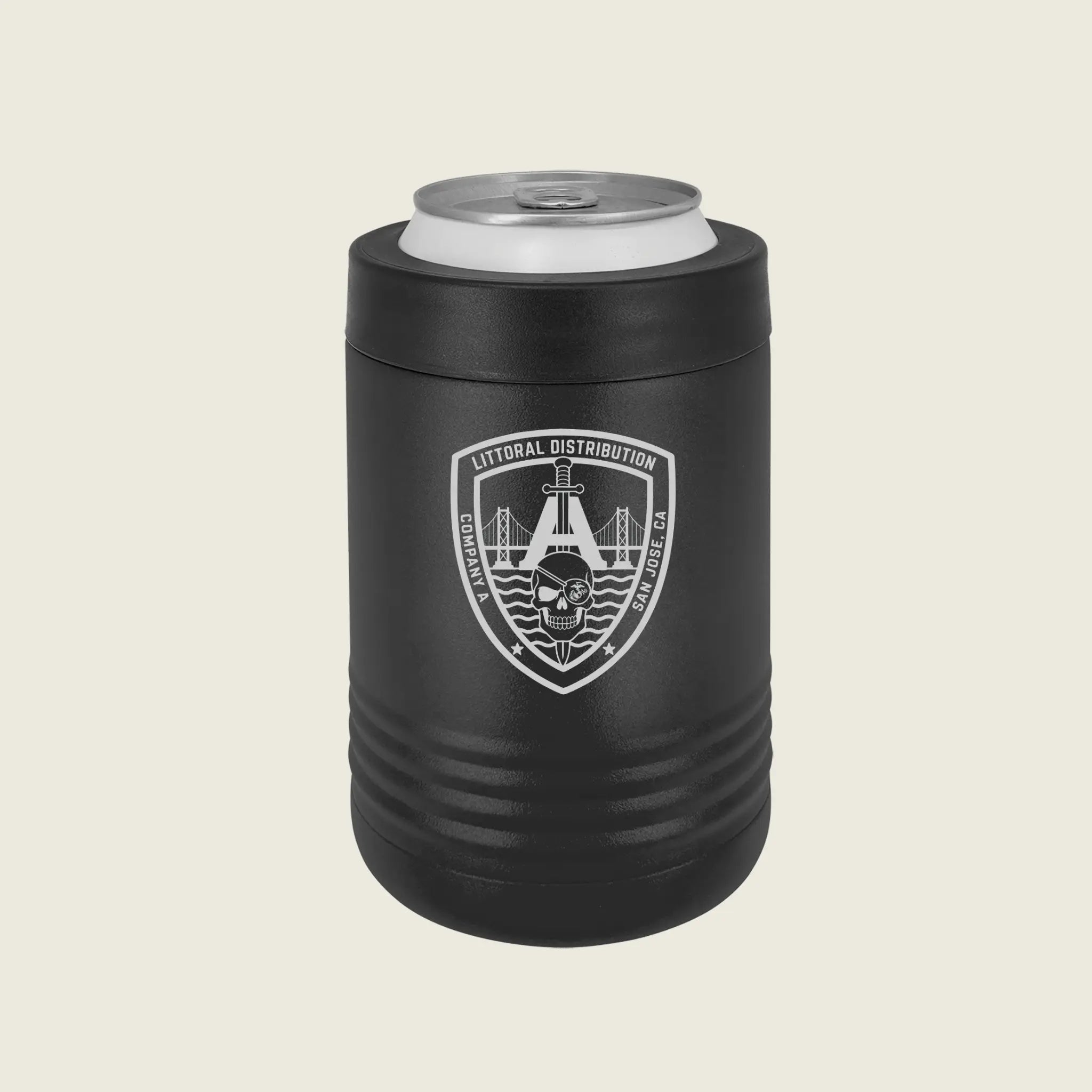 A matte black insulated can cooler sleeve holding a silver aluminum can, featuring a white shield emblem with a bridge, skull, on a light beige background.