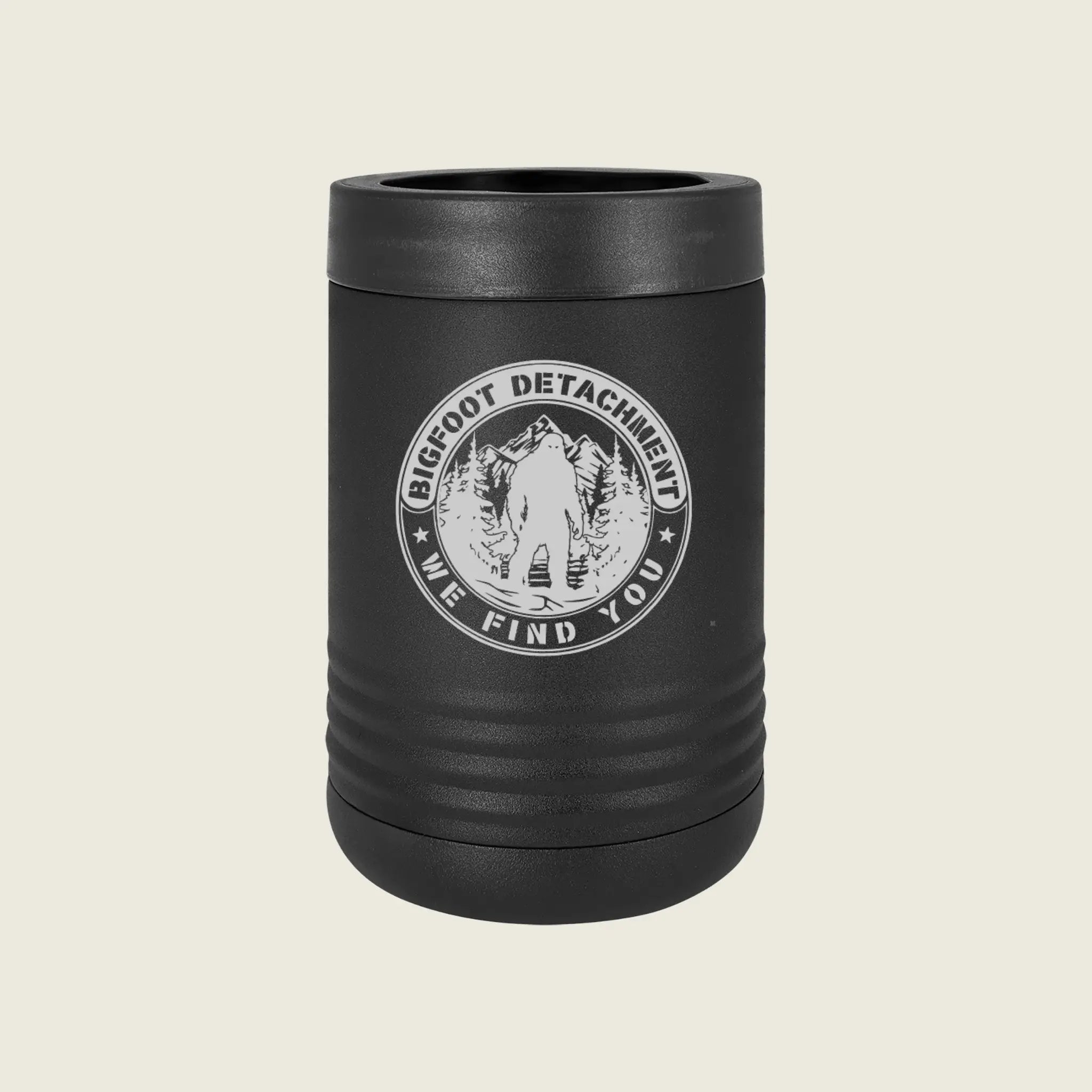 A matte black can cooler with a ribbed design and a white circular 'Bigfoot Detachment We Find You' emblem on the front, set against a solid light beige background.
