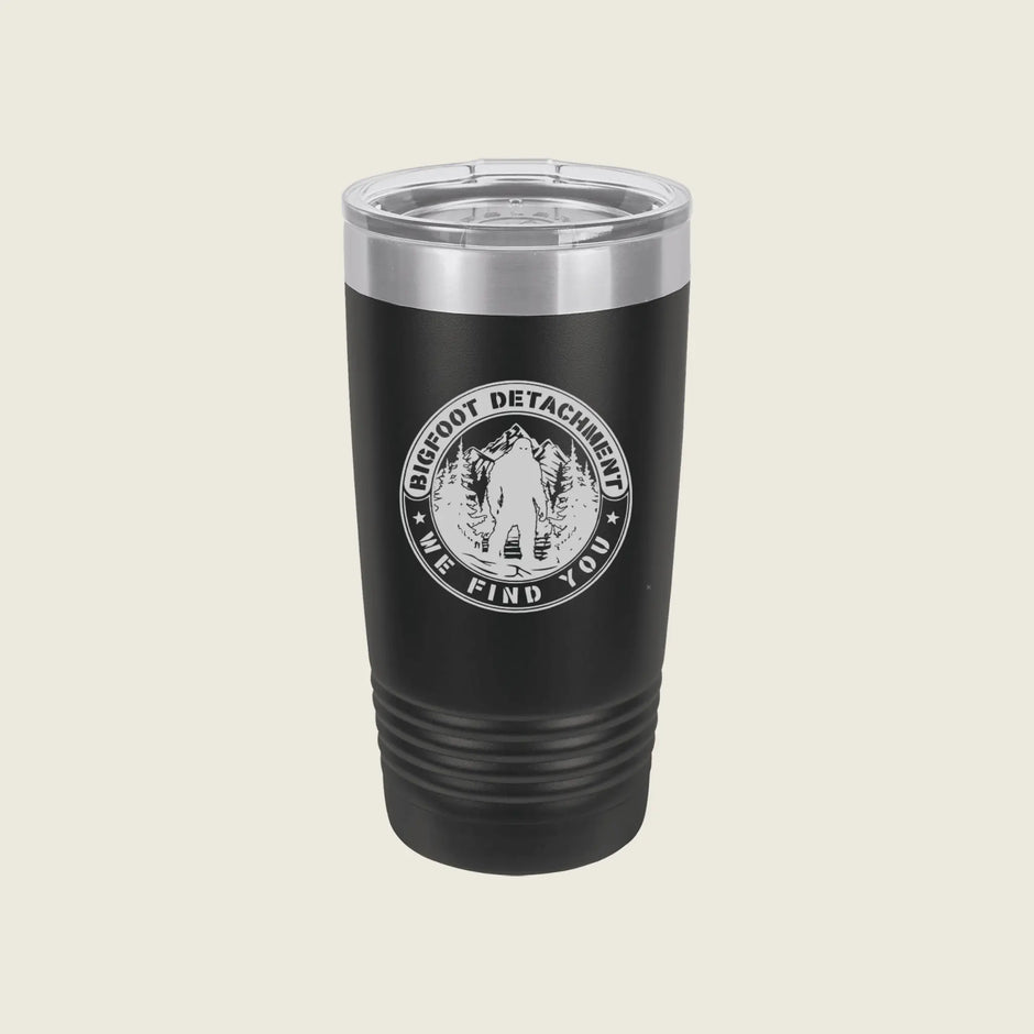 A black insulated travel tumbler with a clear lid, featuring a circular white graphic that reads 'BIG FOOT DETACHMENT WE FIND YOU' around an illustration of a person in a forest.