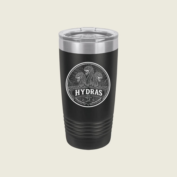 A black insulated travel tumbler with a clear lid, featuring a circular silver graphic of two horses and the word 'HYDRAS' on the front, set against a solid light beige background.