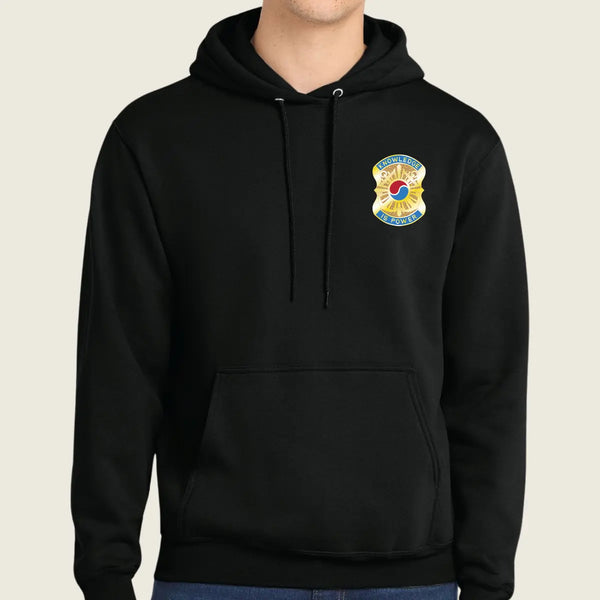 Black hoodie with a colorful emblem on the chest against a beige background