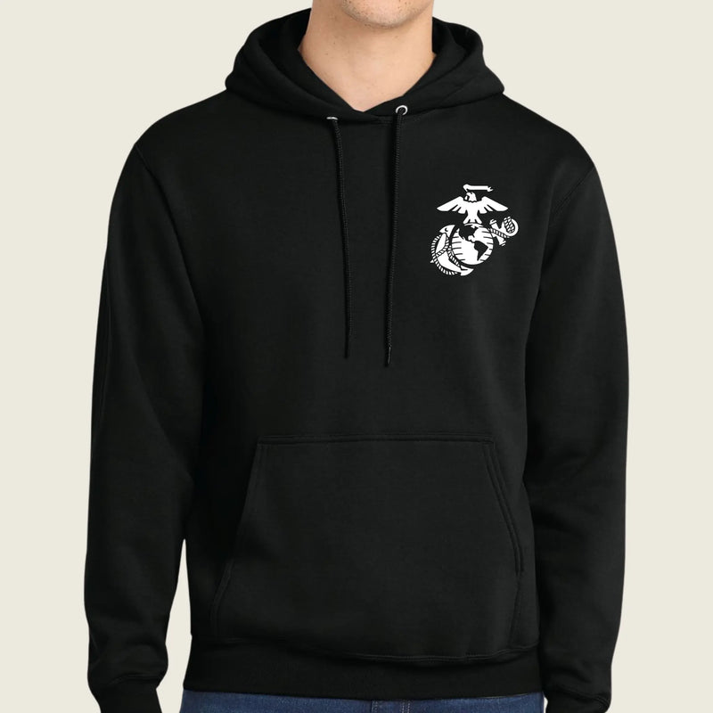 A black pullover hoodie with a white US Marine Corps Eagle, Globe, and Anchor emblem printed on the left chest, worn by a model against a light beige background.