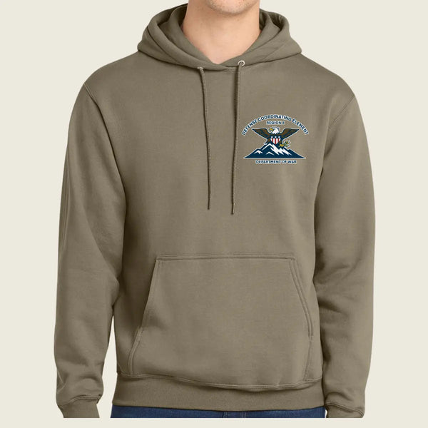 A person wearing a muted olive-brown pullover hoodie with a drawstring hood and kangaroo pocket, featuring a small embroidered United States Army Special Forces crest on the left chest, against a plain light beige background.