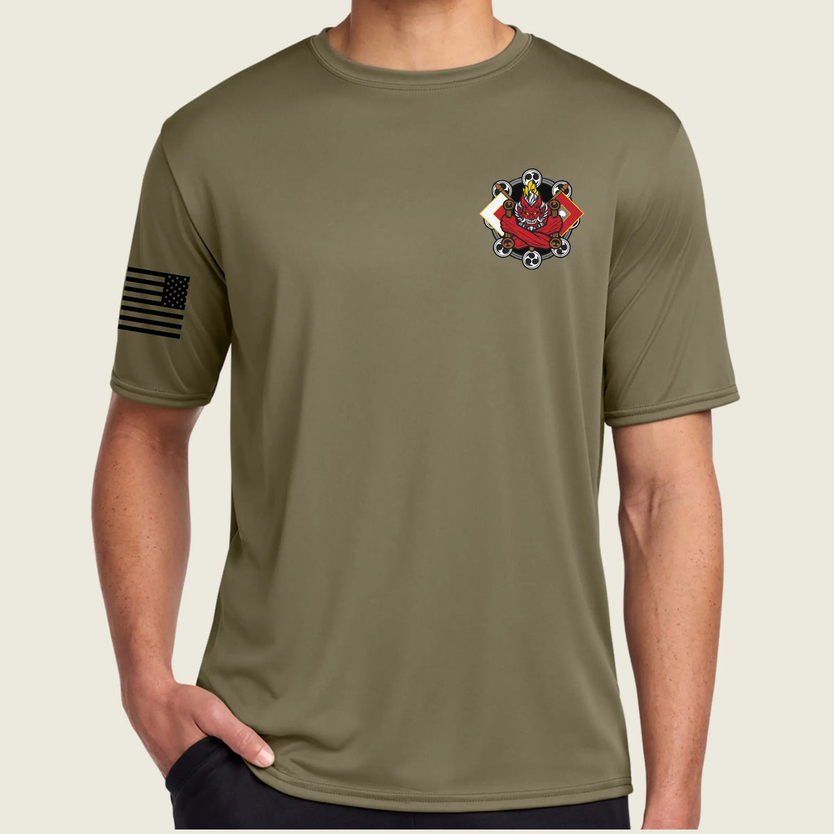 An tan short-sleeve athletic t-shirt worn by a model. The shirt features a black American flag graphic on the right sleeve and a red and gold tactical crest on the left chest.