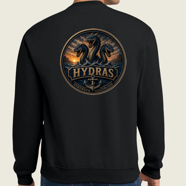 A person wearing a black crewneck sweatshirt, viewed from the back. The sweatshirt features a large circular graphic print on the back depicting three sea monsters in a sunset scene with the word 'HYDRAS' and the phrases 'STRENGTH' and 'Multiplied' below.