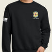 A black crewneck sweatshirt worn by a model, featuring a yellow and army emblem with 'CALL SIGN' text on the left chest and a black-and-white American flag graphic on the right sleeve.