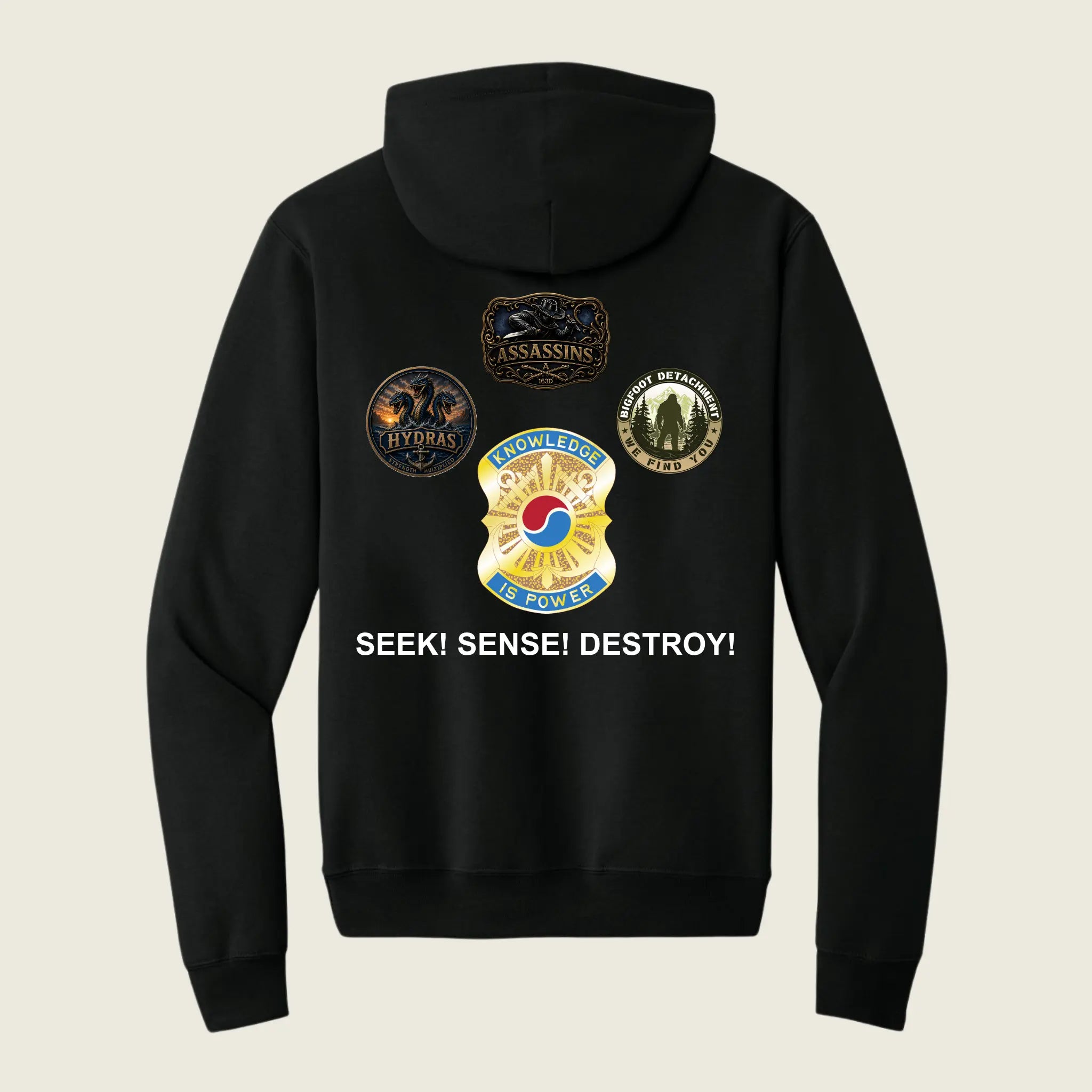 A black zip-up hoodie shown from the back, featuring four military-style insignia patches and the text 'SEEK! SENSE! DESTROY!' printed in white. The background is a solid light beige color.